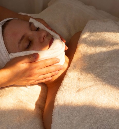 A client relaxing during a warm towel facial treatment at The MH Skin Club